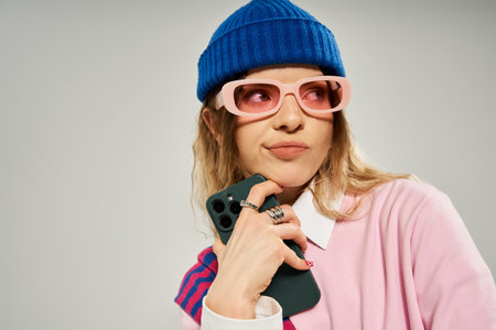 A pretty woman in a trendy outfit holds her phone while striking a playful pose in a studio.