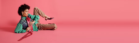 A stylish young woman poses elegantly in a chic outfit against a bright pink backdrop.