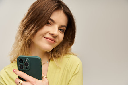 A cheerful young woman dressed in a stylish outfit confidently holds her smartphone, exuding charm.