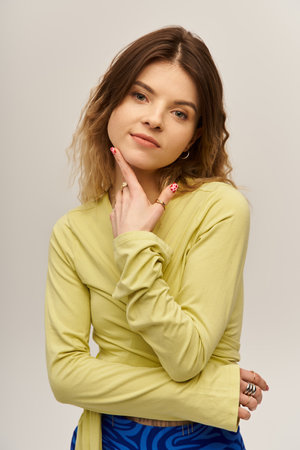 Charming young woman showcases her unique fashion sense with an elegant pose on a grey backdrop.