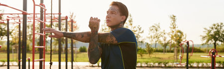A young man is stretching his arms during a refreshing walk in a sunlit park filled with trees.