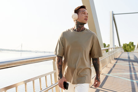 A confident young man strolls peacefully along the riverside walkway, soaking up the sun.