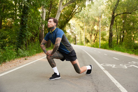 A handsome young man stretches on a peaceful pathway lined with trees, enjoying nature and fitness.の写真素材
