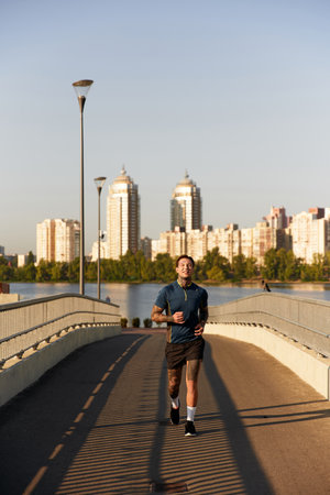 A young man jogs joyfully by the waterfront on a beautiful day amidst the cityscape.の写真素材