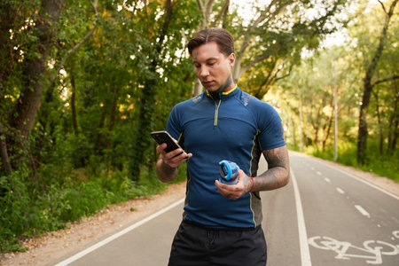 Handsome young man takes a stroll on a tree lined path, engaged with his smartphone.