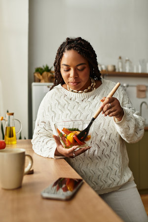 A young African American woman prepares a vibrant salad in her cozy kitchen, savoring the moment.