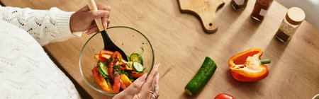 A young african american woman prepares a vibrant salad at home, enjoying the cooking process, bannerの写真素材