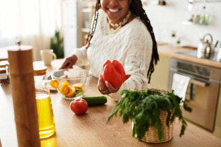 A young Black woman joyfully makes a vibrant salad at home, savoring the cooking process.の写真素材