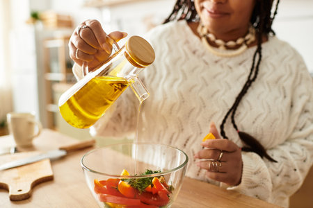 A young Black woman joyfully makes a vibrant salad with fresh ingredients in her kitchen.の写真素材