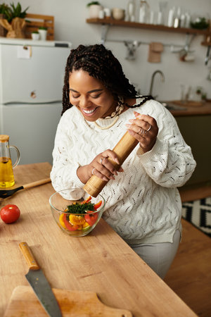 A cheerful young African American woman is making a vibrant salad at home with fresh ingredients.