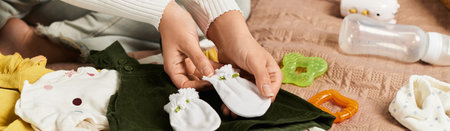 A young woman delicately arranges tiny baby clothes and accessories on a soft blanket.