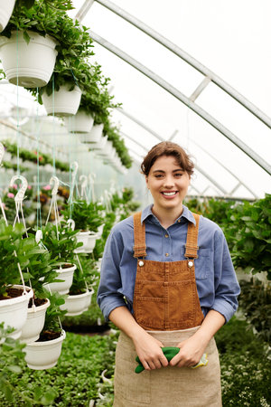 A joyful young woman tending her flourishing plants in a cozy greenhouse.の写真素材