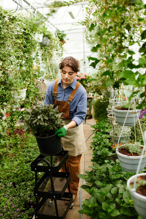 In a lush greenhouse, a young woman nurtures her plants with joy and dedication.