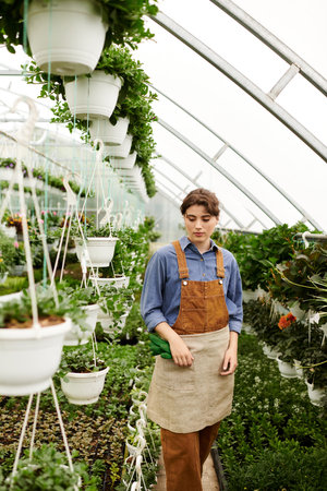 A young woman skillfully tends to her potted plants in a thriving greenhouse, basking in bliss.の写真素材