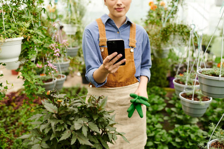 A young woman enjoys nurturing her plants in a sunlit greenhouse filled with greenery.の写真素材