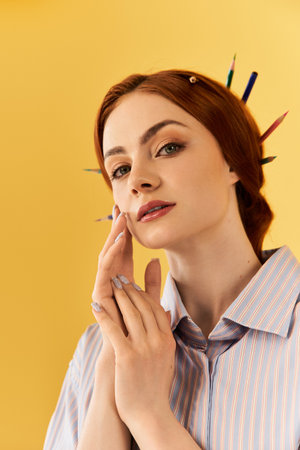 A young woman with colorful pencils in her hair gently touches her cheek against a yellow backdrop.