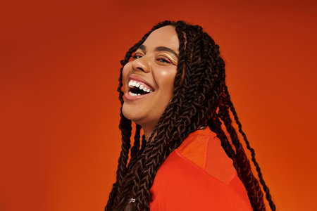 A joyful young woman with braids poses in a vibrant outfit, showcasing her cheerful spirit.