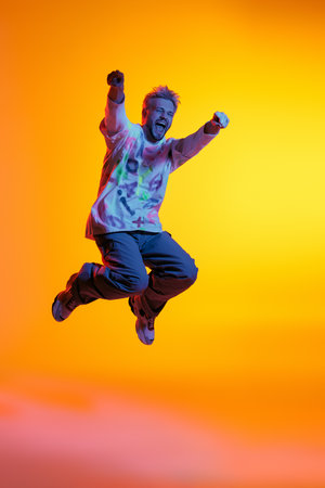 A handsome young man leaps in the air with excitement, embracing a bright and colorful backdrop.