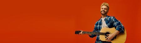 A joyful young man strums his guitar, smiling against a bright orange background.