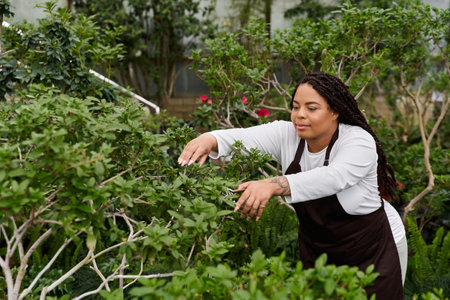 An African American woman with braids cares for vibrant plants in a lush greenhouse setting.