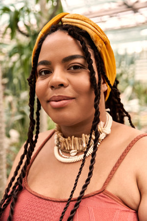 A joyful Black woman with braids relaxes in a tranquil greenhouse filled with greenery.