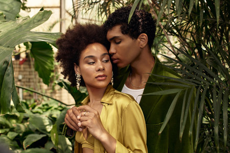 A loving couple shares a tender moment surrounded by flourishing plants in a greenhouse setting.の写真素材