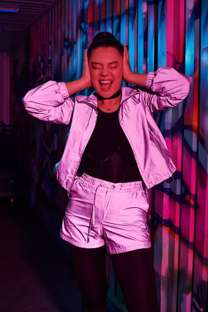 A joyful woman in a shiny outfit dances against a colorful city backdrop at night.の写真素材