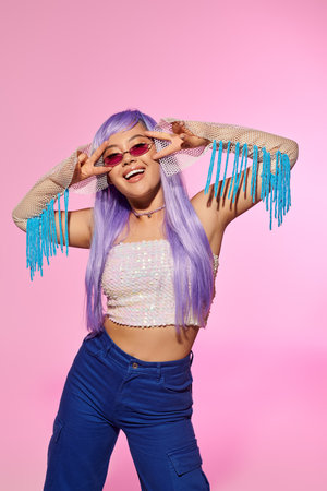 Woman in trendy outfit shows playful energy, smiling broadly while posing in a colorful setting.