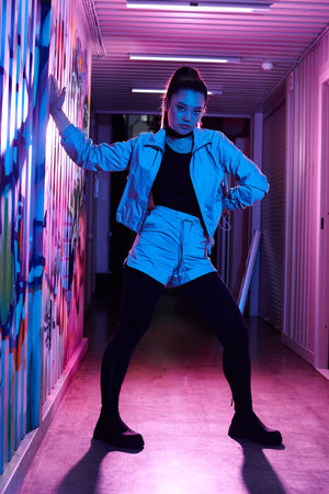A fashionable woman strikes a powerful pose in a colorful alleyway adorned with street art.の写真素材