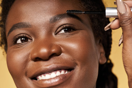 A young black woman with radiant skin applies beauty products while smiling in a studio.