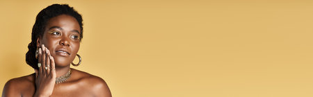 Young woman with glowing skin gently touches her face in an artistic studio background, bannerの写真素材