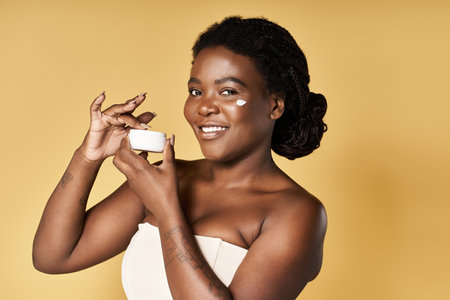 A young Black woman shares her beauty routine with a skincare product in a bright studio.の写真素材
