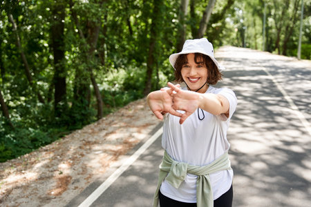 A cheerful young woman enjoys her outdoor workout, stretching amidst lush greenery.