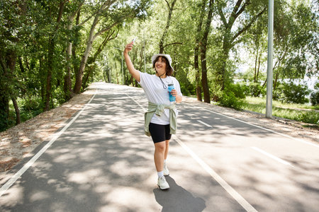 Smiling young woman exercises along a tree-lined path, embracing a healthy outdoor lifestyle.