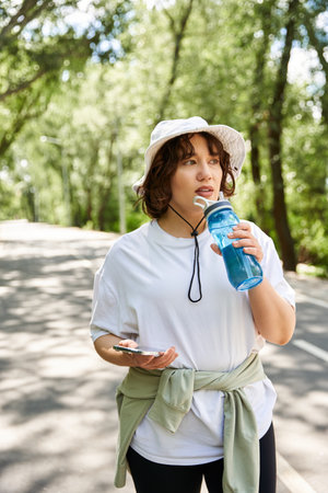 A young woman pauses her exercise routine outdoors, sipping water while staying hydrated.