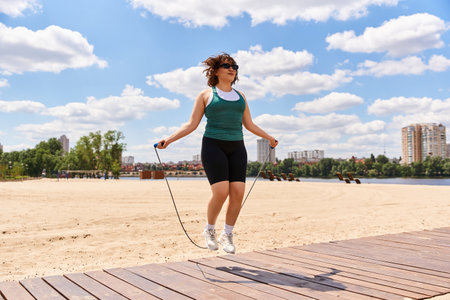 Young woman enjoys a fitness routine outdoors, skipping rope in the warm sun by the water.
