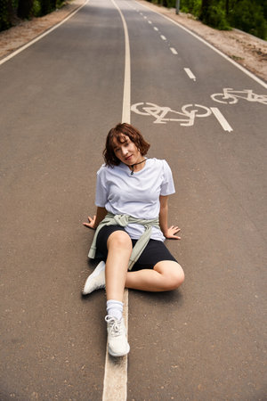 A young woman enjoying a sunny day outdoors, seated on a peaceful street, embracing summer bliss.の写真素材