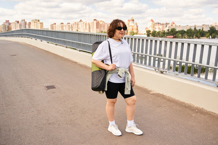 Fit woman dressed for exercise walks along a riverside path in a vibrant urban setting.