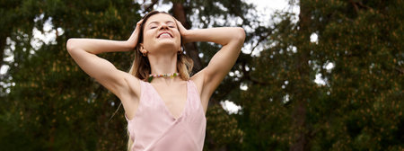 A young woman with arms raised above her head smiles contentedly under the trees on a bright day.