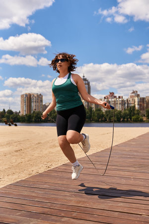 Fit young woman exercises with a jump rope on a beautiful sandy beach under a clear sky.の写真素材