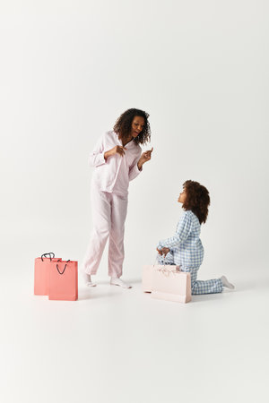 Mother and daughter, both in matching pajamas, gleefully unpack presents in a studio setting.の写真素材
