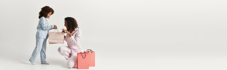 An African American mother and daughter, in matching pyjamas, are going through their shopping bags,...