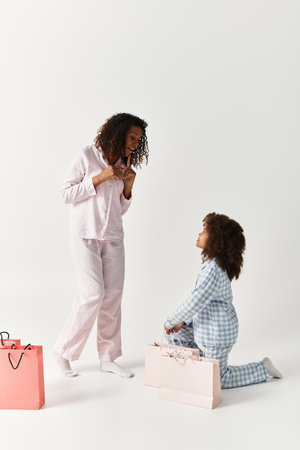 An African American Mother and daughter, both in matching pajamas, pose in a studio next to shopping bagsの写真素材