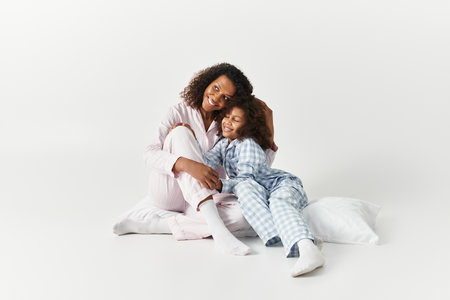 A happy African American mother embraces her joyful daughter in pyjamas in a studio setting.の写真素材