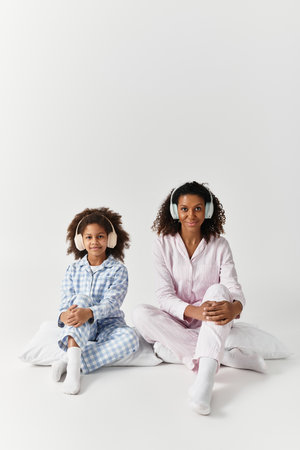 Black mom and daughter in matching PJs listen to music.の写真素材
