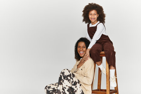 A mother and daughter express joy and style while posing in fashionable outfits in a studio.