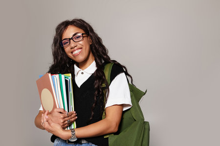 A confident young student holds books, radiating joy in a casual setting.の写真素材