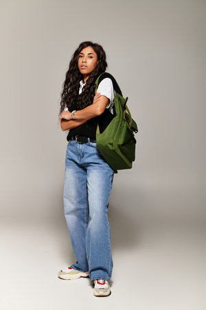 A confident young woman showcases her trendy student style while standing with a backpack.