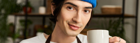 Young man takes a break with a mug in hand while transplanting vibrant plants in a bright studio.