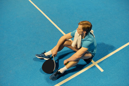 A young athlete rests on the court after an intense game of padel. He reflects on his performance.の写真素材